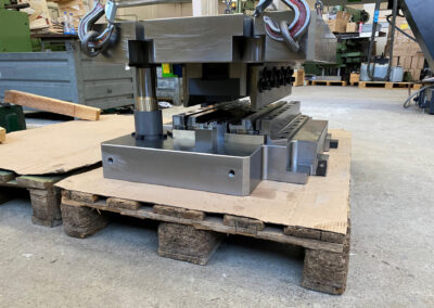 Ein massives, zweiteiliges Biegewerkzeug liegt auf einer Holzpalette, geschützt durch eine Kartonunterlage, auf dem Werkstattboden.