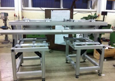 Ein großes, im Aufbau befindliches Maschinengestell aus silbernen Aluminium-Systemprofilen steht in einer Werkstatt mit Backsteinwänden.