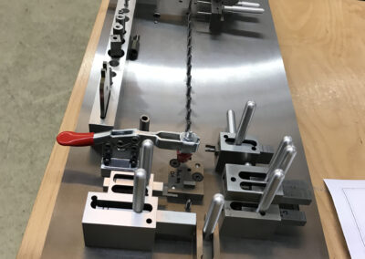 Eine kundenspezifische Prüfvorrichtung (Lehre) auf einer massiven, geschliffenen Metallgrundplatte steht auf einem hölzernen Arbeitstisch.