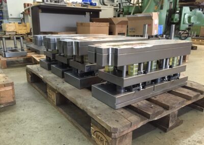 Mehrere schwere, fertig montierte Loch- oder Stanzwerkzeuge aus massivem Stahl stehen auf einer hölzernen Transportpalette in einer Werkhalle.