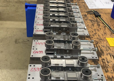 Eine lange Reihe identischer, präzise gefertigter Metall-Baugruppen steht hintereinander auf einer abgenutzten hölzernen Werkbank.